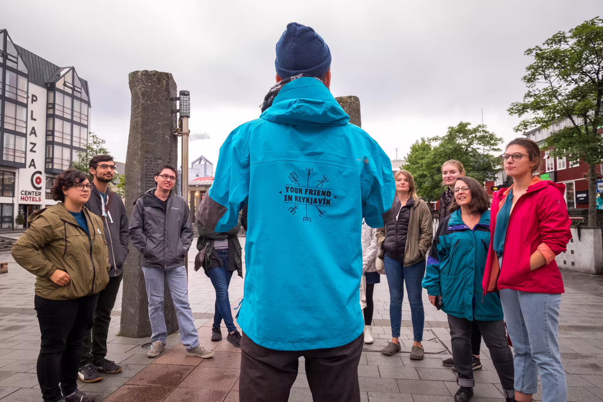 Tour guide in blue Reykjavik jacket addresses small group of tourists in city square