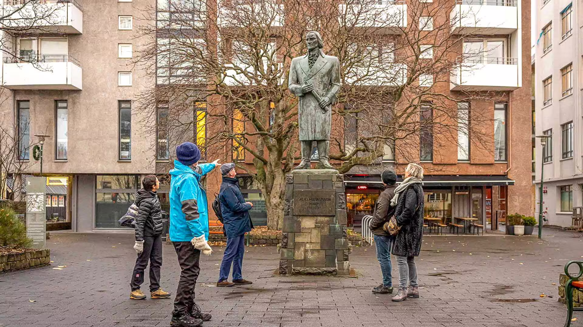 Tour guide pointing at Skúli Magnússon statue during Reykjavik walking tour with small group of tourists