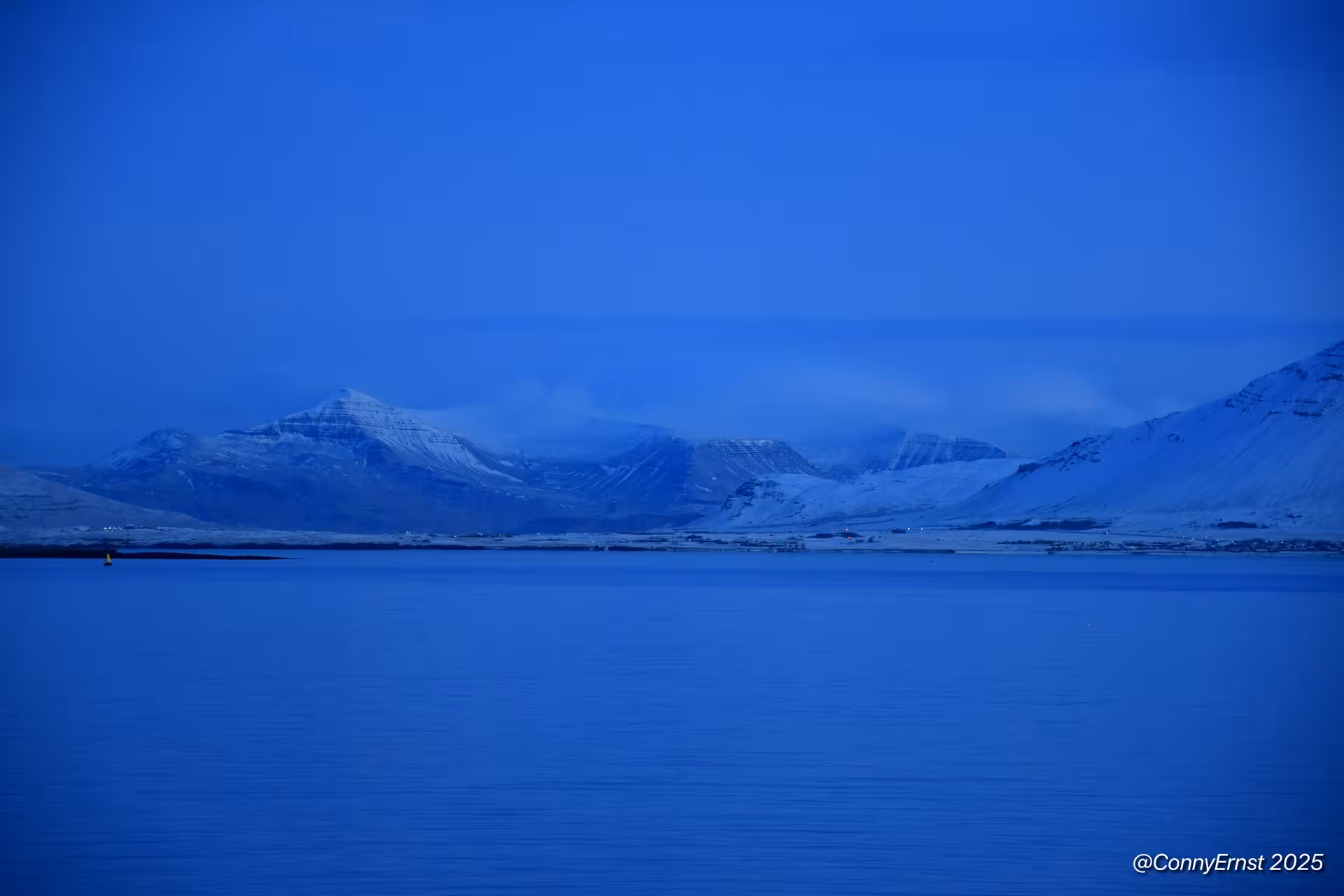 Snow-capped mountains reflecting over calm blue waters near Reykjavik at dusk