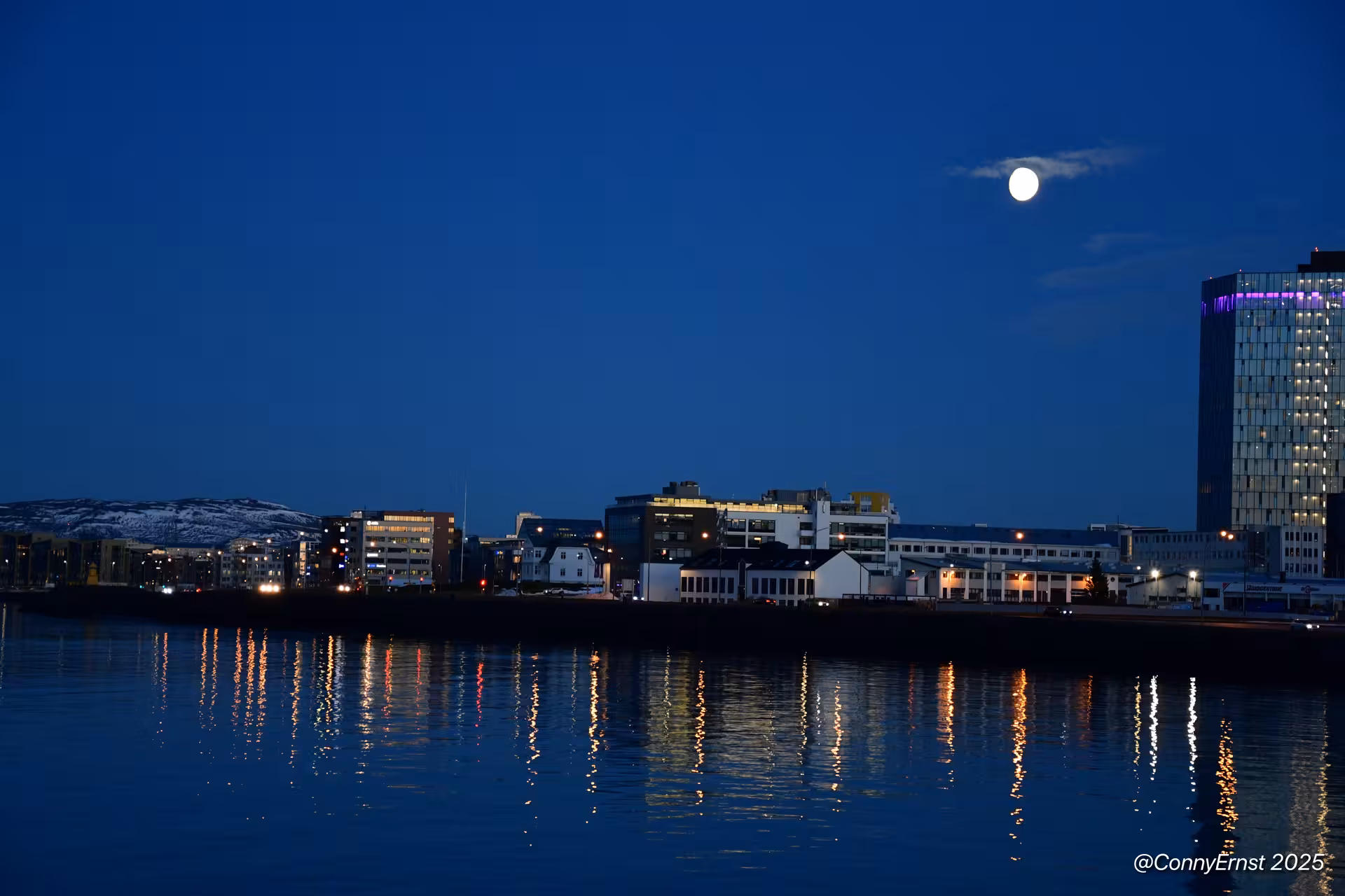 Reykjavik city waterfront skyline at night with full moon reflecting on calm harbor waters