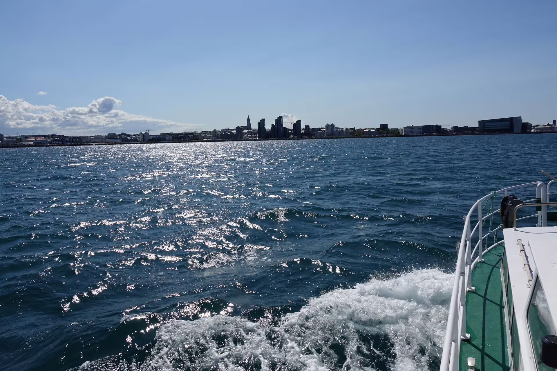 View from whale watching boat stern with Reykjavik city skyline across sparkling blue harbor waters