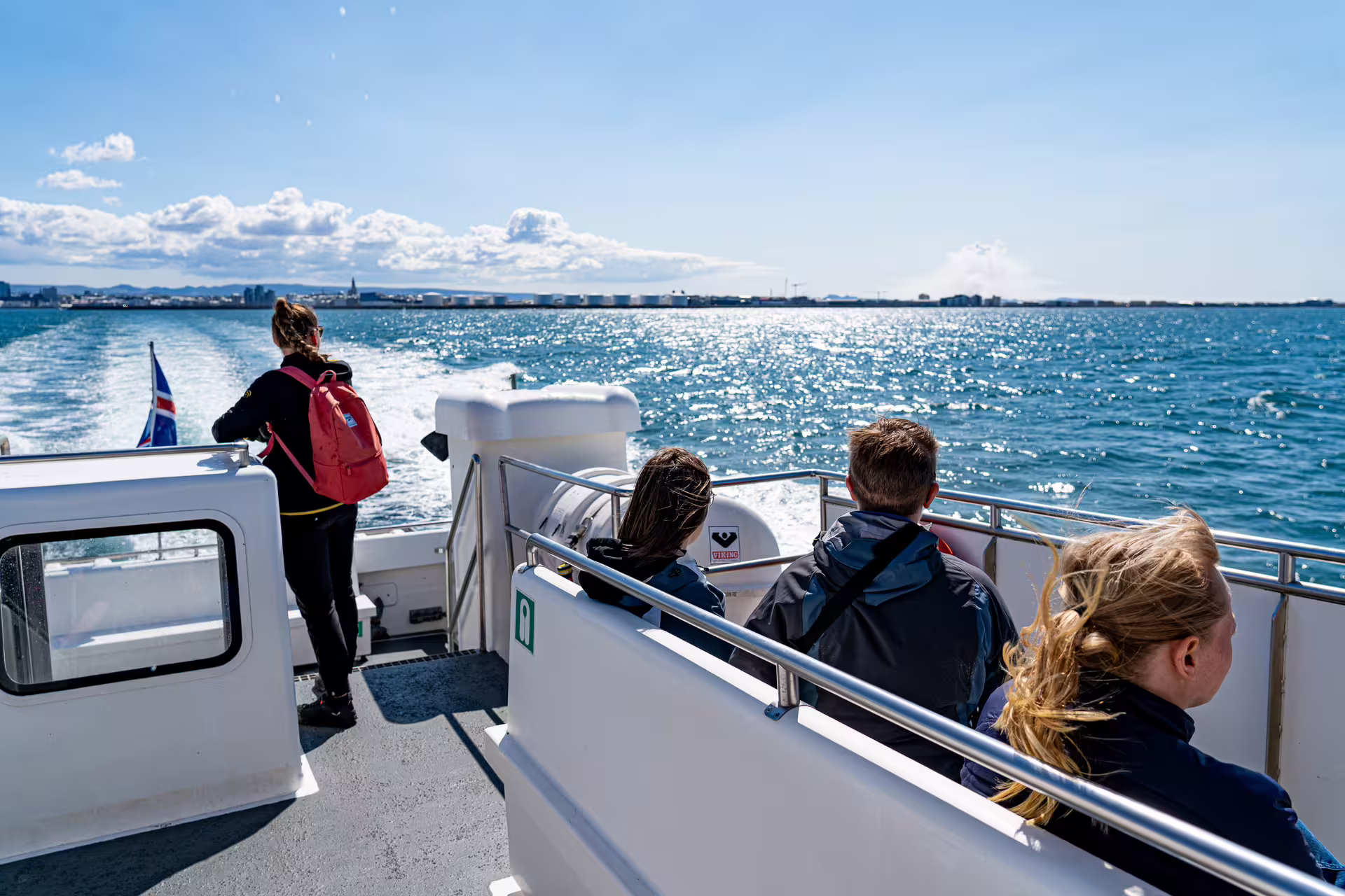 Passengers on boat deck watching Reykjavik coastline during whale watching tour from Old Harbour