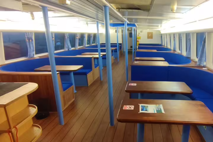Empty blue booth seating and wooden tables inside a whale watching cruise ship cabin