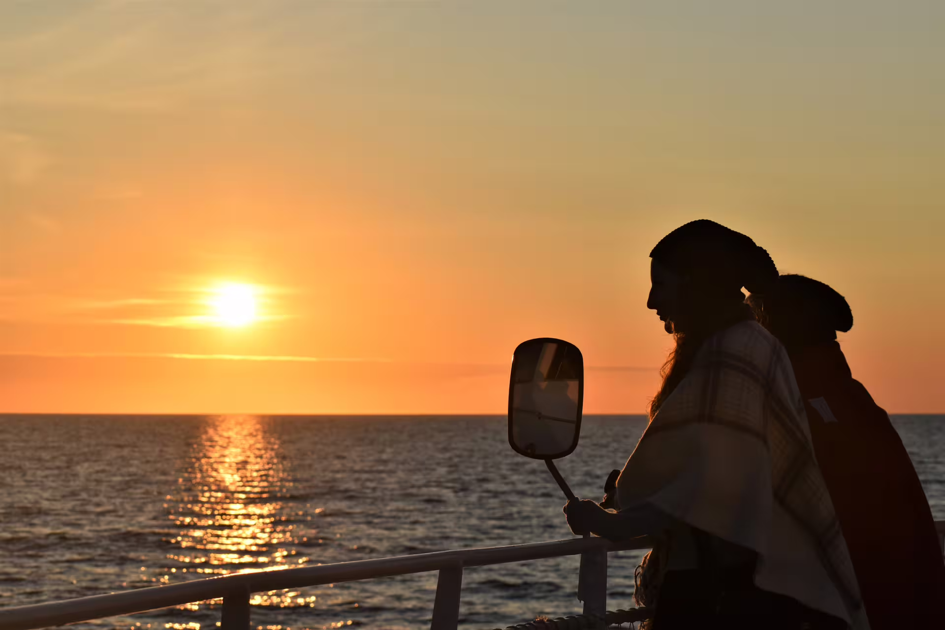 Silhouette of passengers on deck watching midnight sun over ocean during Reykjavik whale watching boat tour