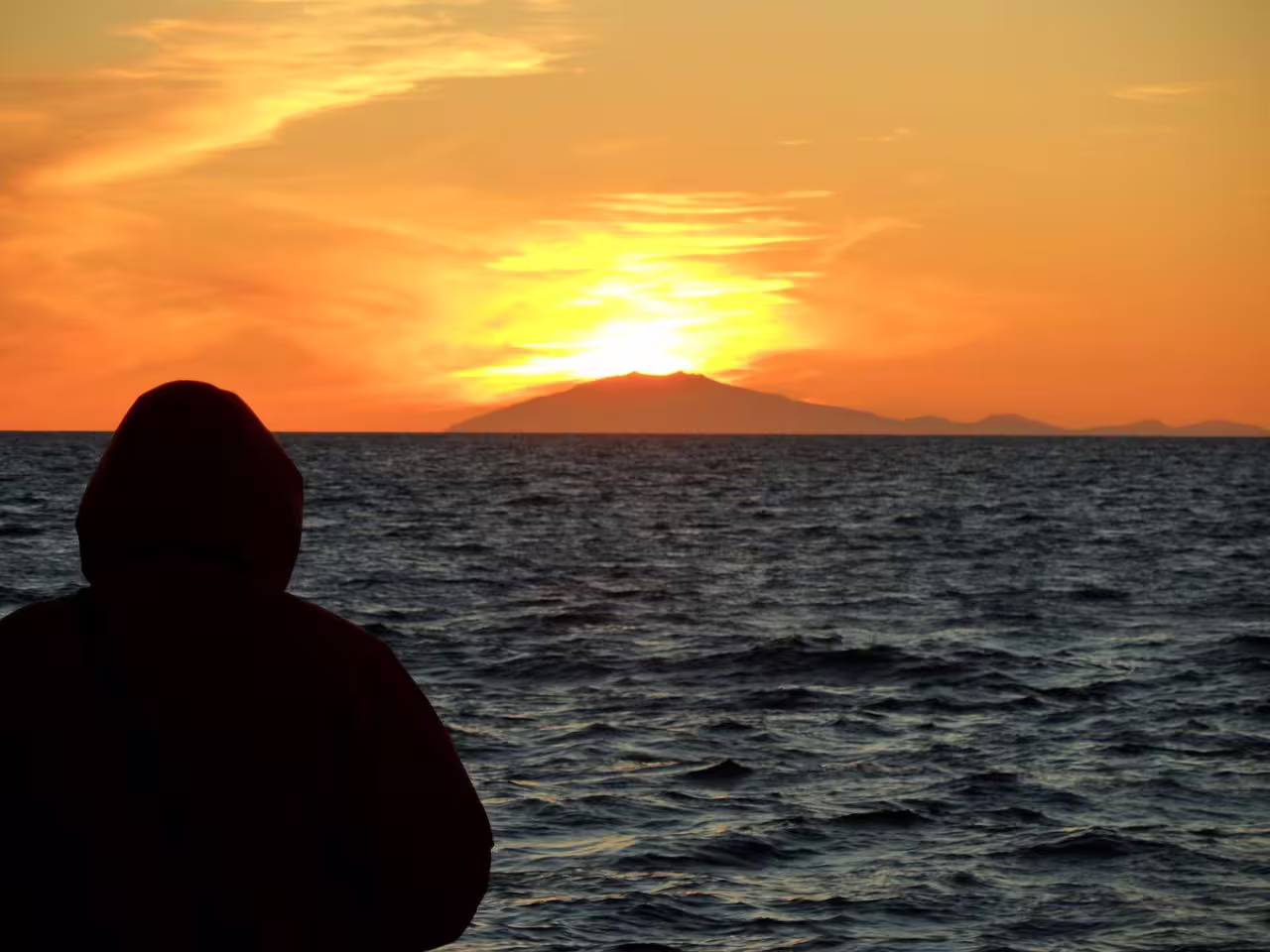 Silhouette of person watching midnight sun set over volcanic island during Reykjavik whale watching boat tour