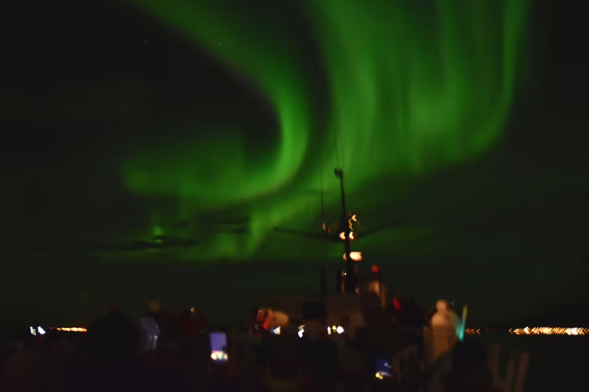 Vibrant green northern lights aurora borealis swirling over a whale watching boat in Reykjavik at night