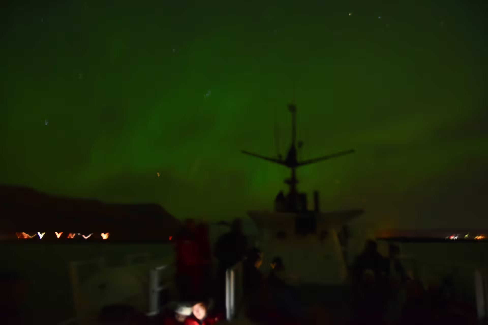 Northern lights glowing green over a whale watching boat in Reykjavik harbor at night