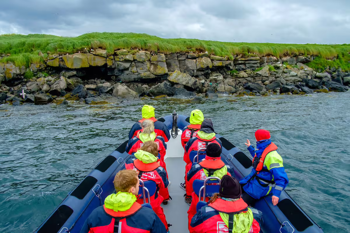 Group of tourists in red life jackets on a RIB boat approaching rocky island cliffs near Reykjavik