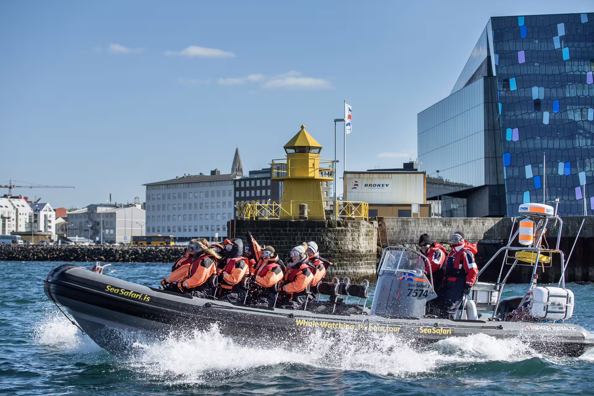Sea Safari RIB whale watching boat speeding through Reykjavik harbor with passengers in orange survival suits