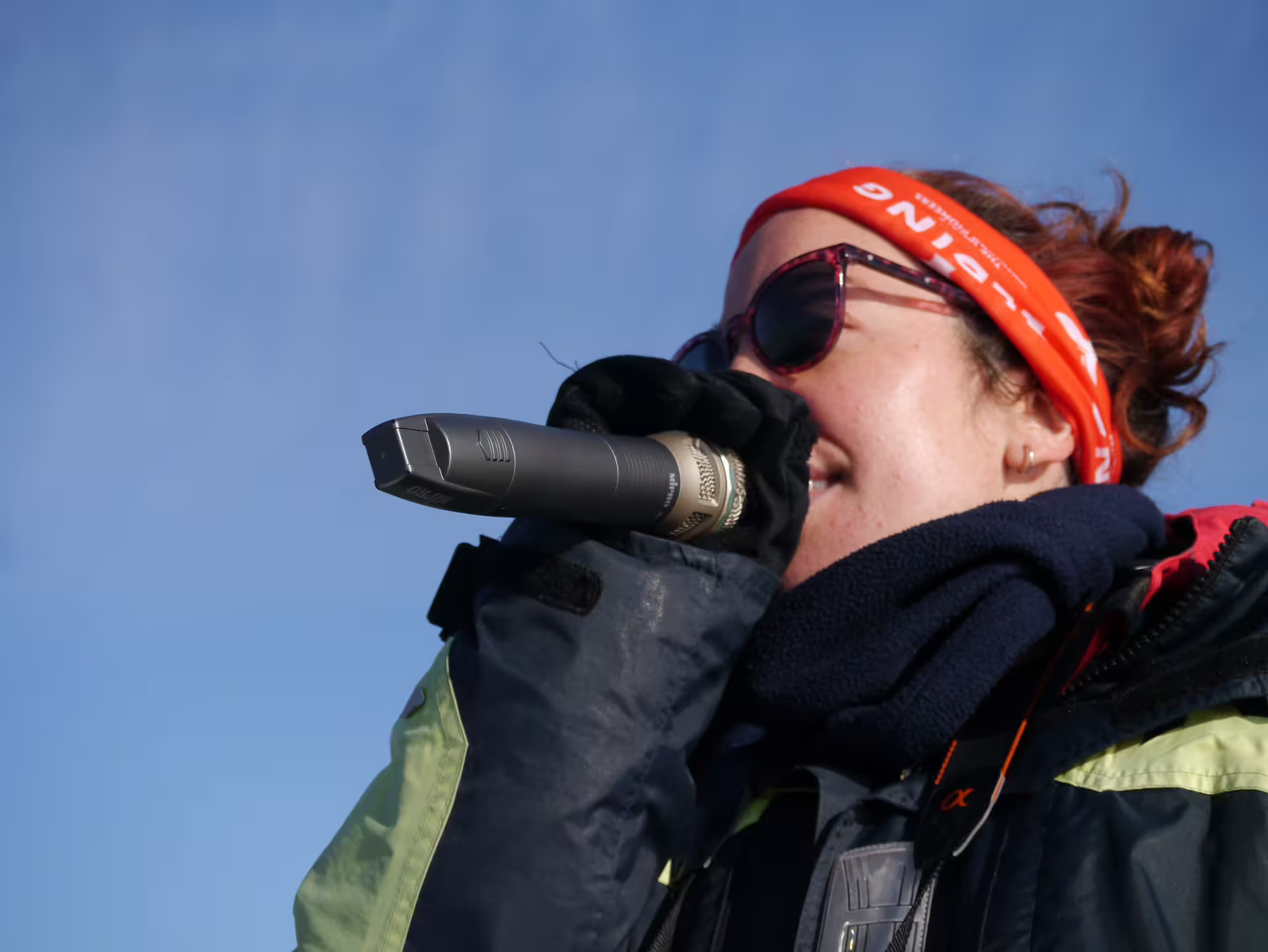 Tour guide speaking into microphone on Reykjavik whale watching boat tour, wearing orange headband and sunglasses