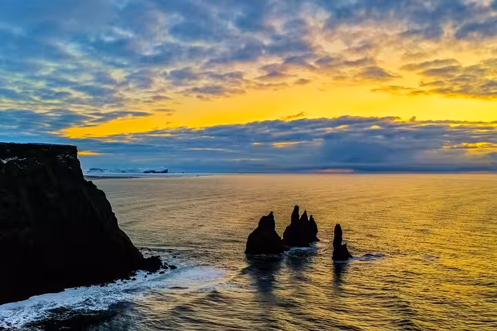 Dramatic sunset over Reynisdrangar sea stacks on Iceland's South Coast with golden sky reflections