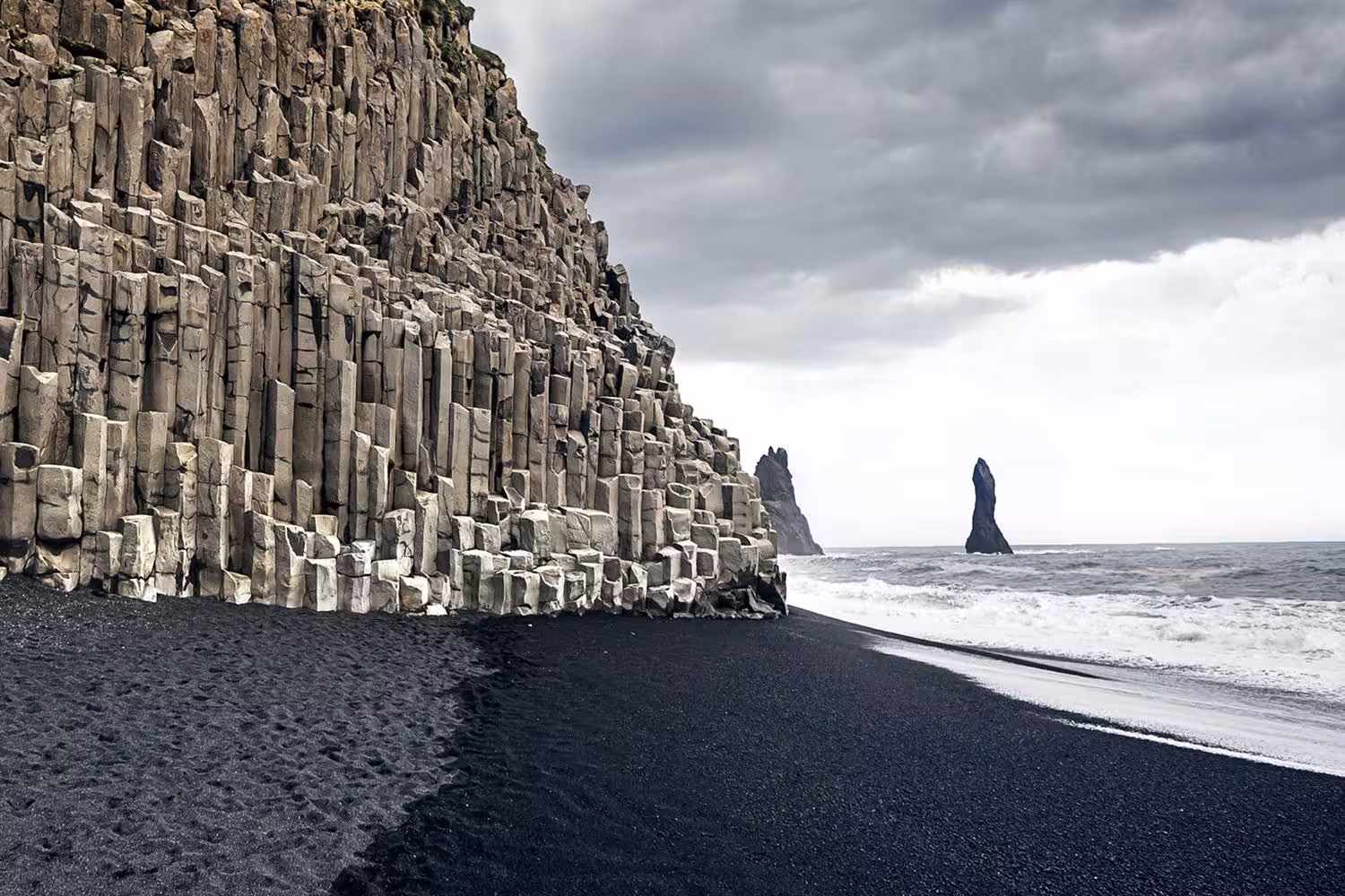 Dramatic black sand beach at Reynisfjara with basalt columns and Reynisdrangar sea stacks on Iceland South Coast tour.