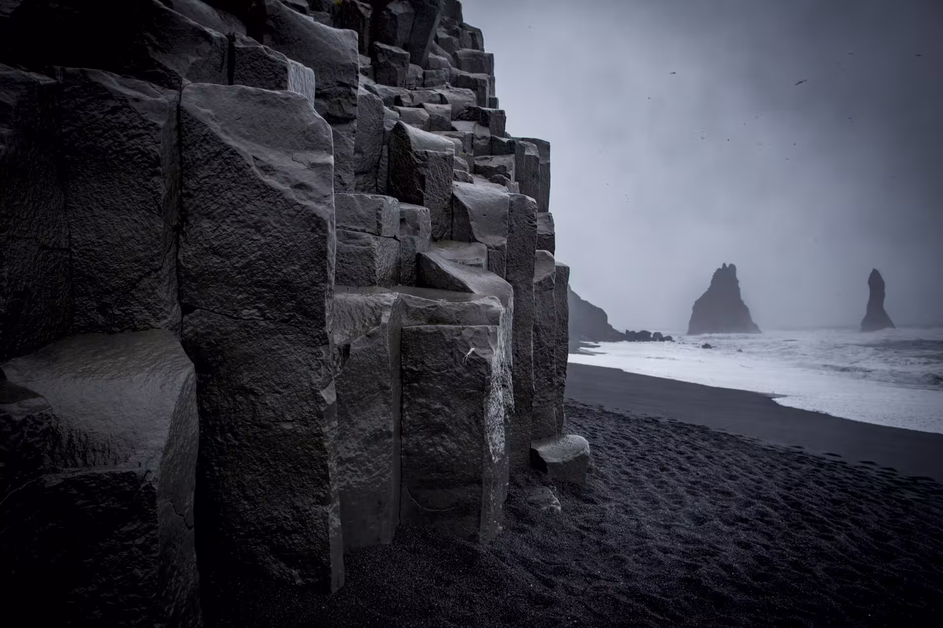 Black basalt columns and volcanic sand beach at Reynisfjara with sea stacks in misty background, Iceland