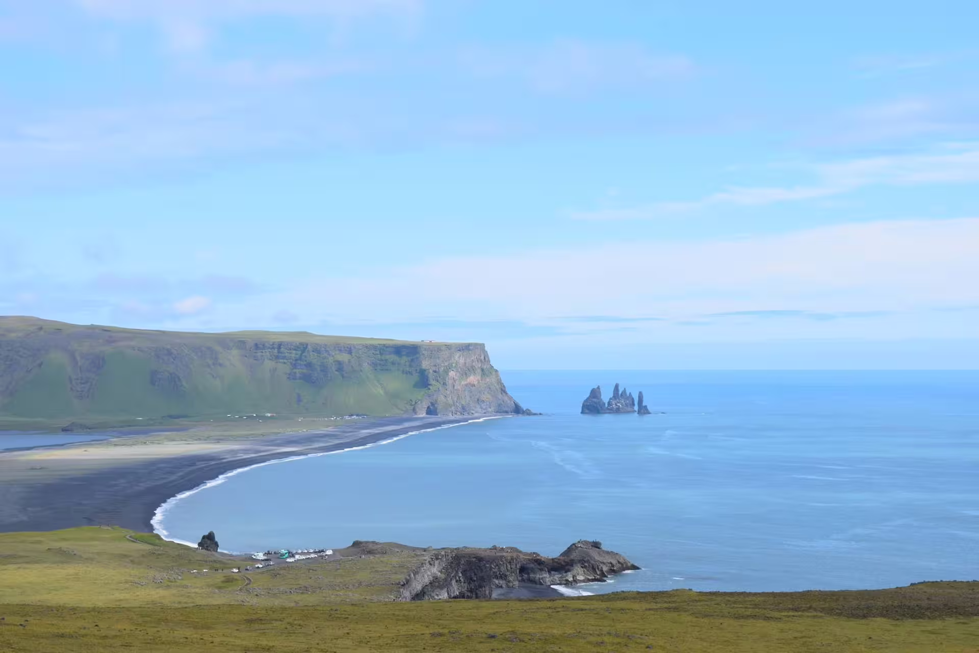 Black sand beach at Reynisfjara with Reynisdrangar sea stacks and green cliffs in Iceland