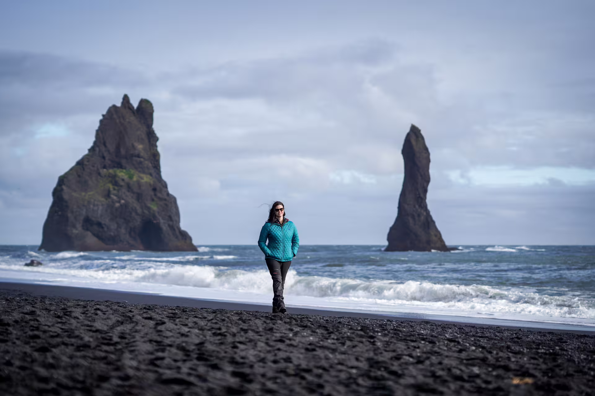 Woman strolling Reynisfjara black sand beach with iconic basalt sea stacks on Iceland South Coast summer adventure