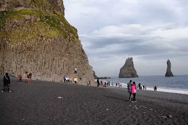 Tourists on Reynisfjara black sand beach with basalt columns and sea stacks on Iceland's south coast