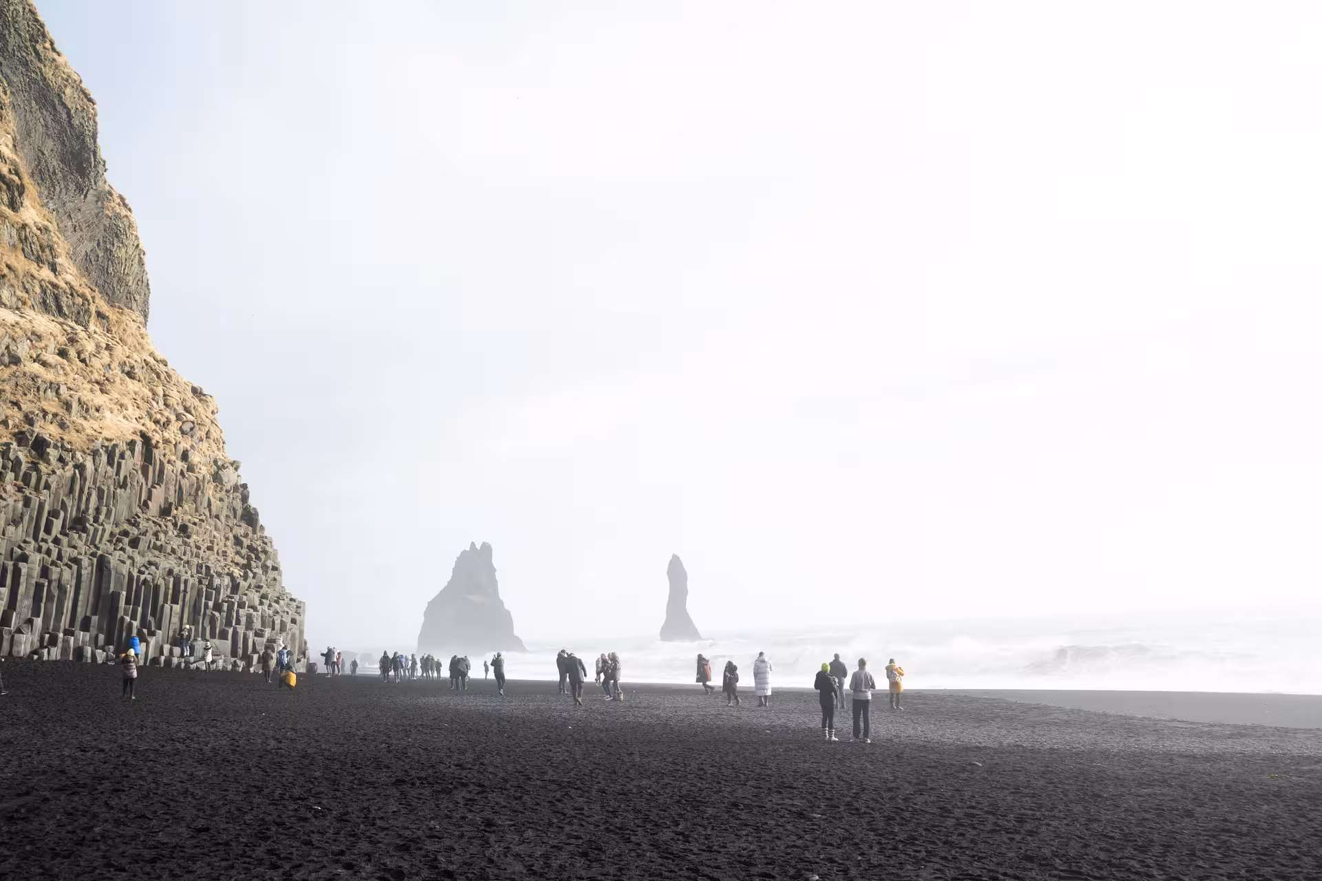 Tourists walking on Reynisfjara black sand beach with basalt columns and sea stacks in Iceland