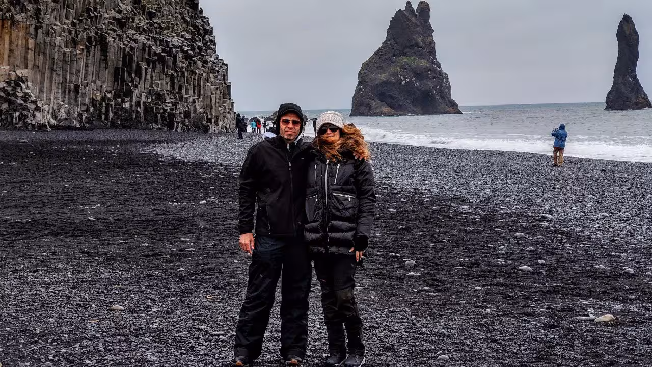 Couple posing on Reynisfjara black sand beach with basalt columns and sea stacks on Iceland south coast