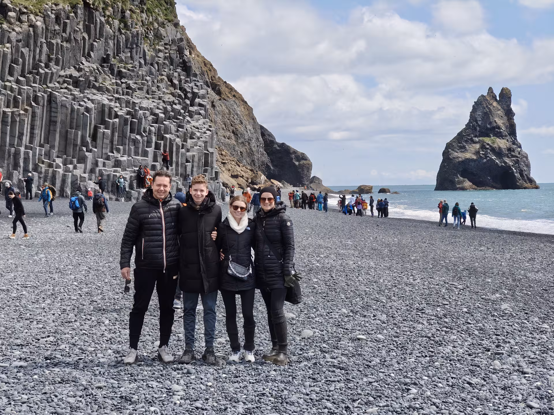 Three tourists posing at Reynisfjara black sand beach with basalt columns and Reynisdrangar sea stacks, Iceland