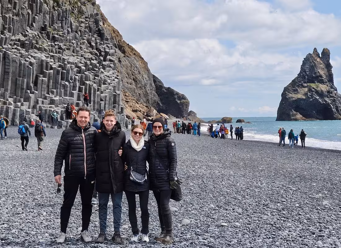 Family of four posing at Reynisfjara black sand beach with basalt columns and sea stacks in Iceland