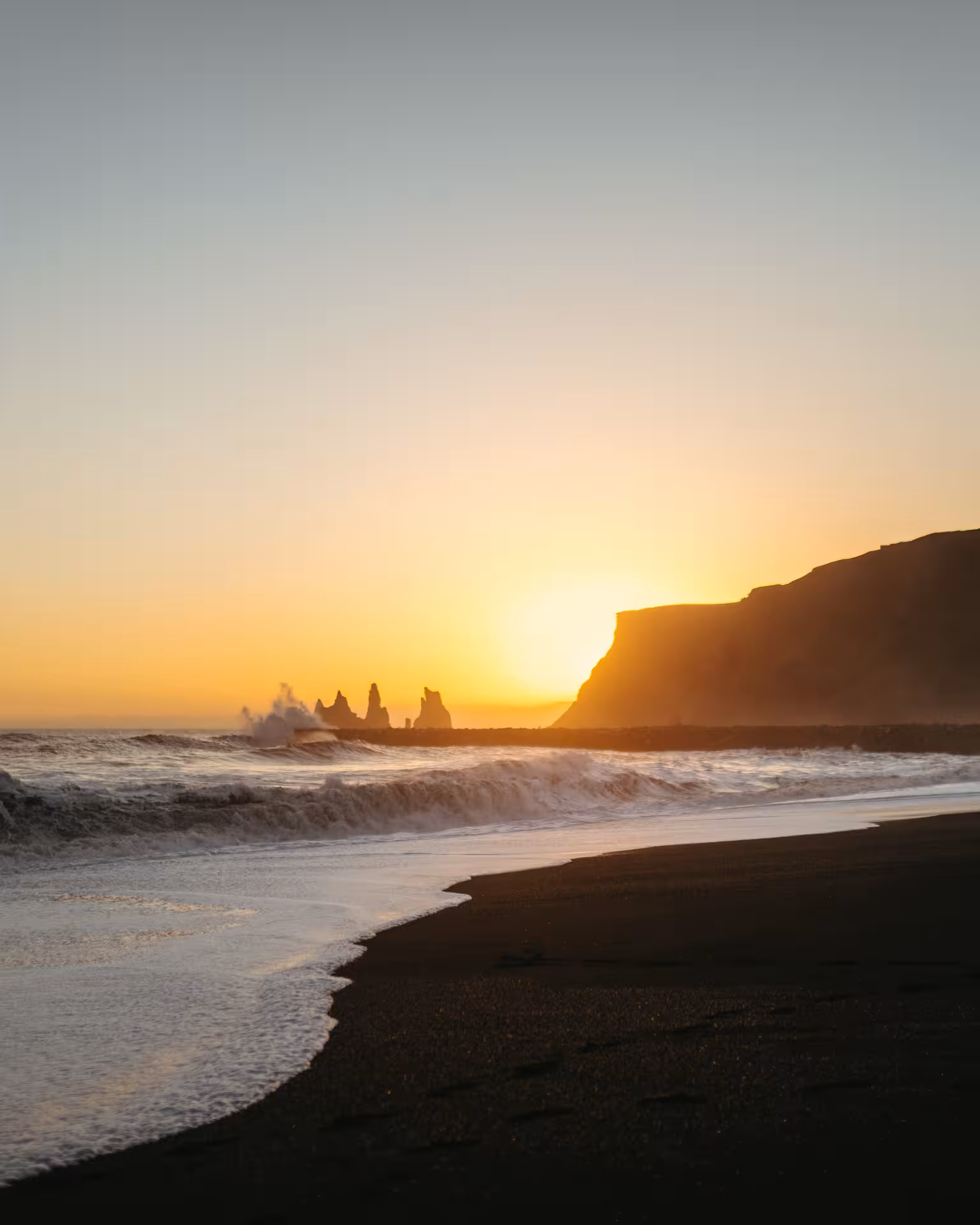 Sunset at Reynisfjara black sand beach with waves and sea stacks, South Coast stop on Sólheimajökull tour