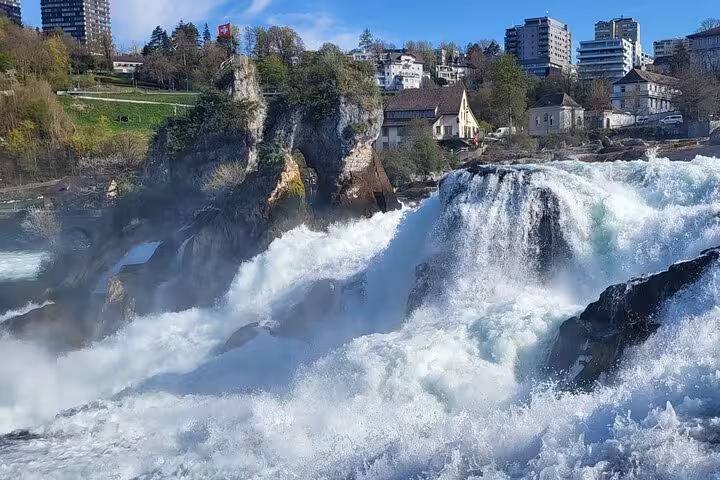 Breathtaking view of Rhine Falls showcasing cascading water surrounded by lush greenery and nearby buildings in Switzerland.