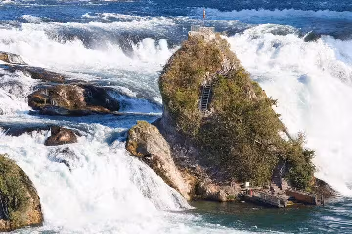 Scenic view of Rhine Falls cascading around a rocky outcrop with lush greenery, perfect for a Zurich day trip adventure.