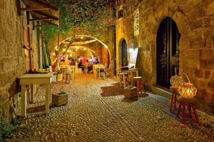 Charming cobblestone alley in Rhodes Old Town lit by warm lights, offering a glimpse into local nightlife and dining.