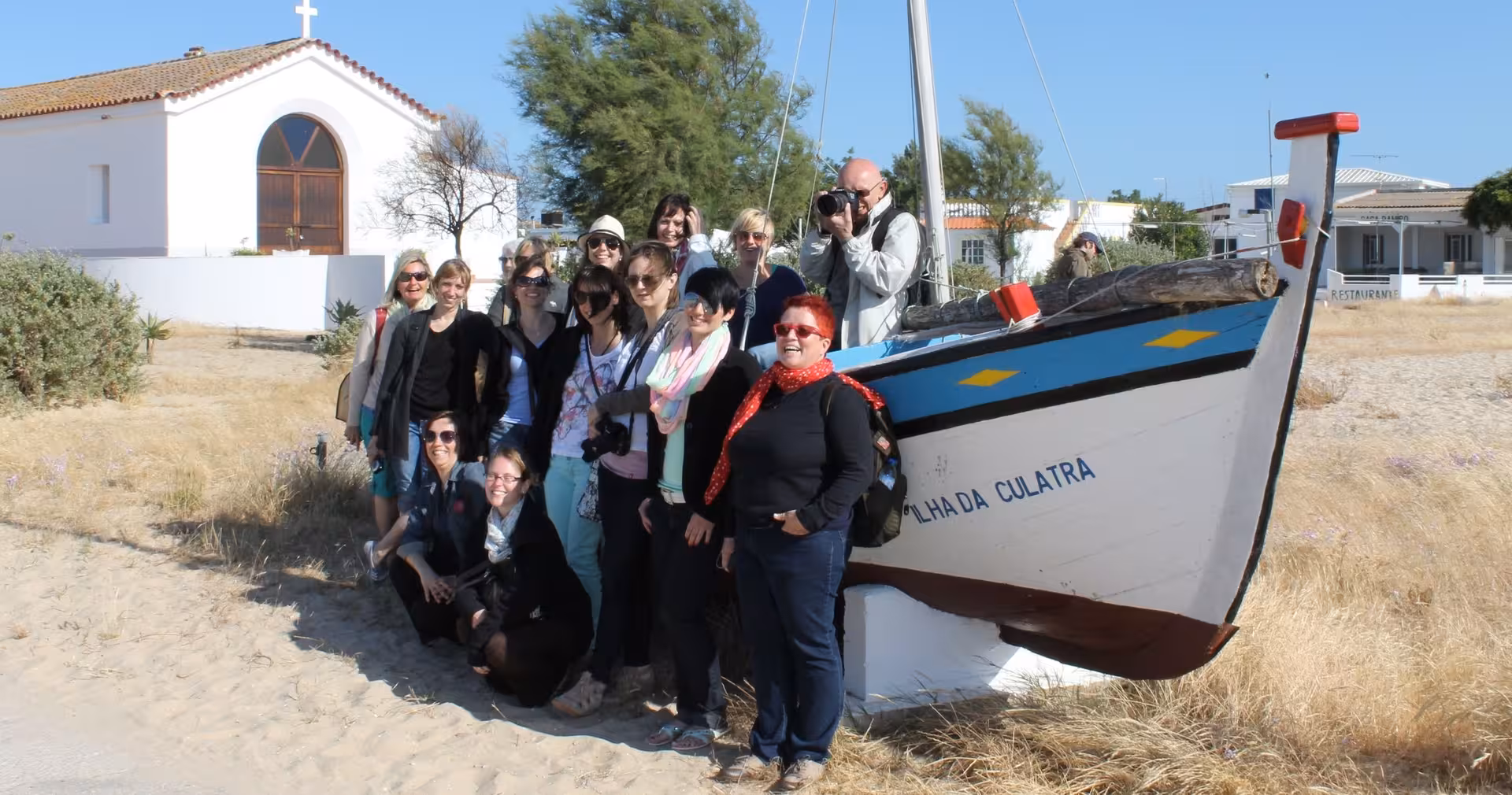Tour group posing beside a traditional Ilha da Culatra fishing boat during a 2-hour Ria Formosa Natural Park excursion
