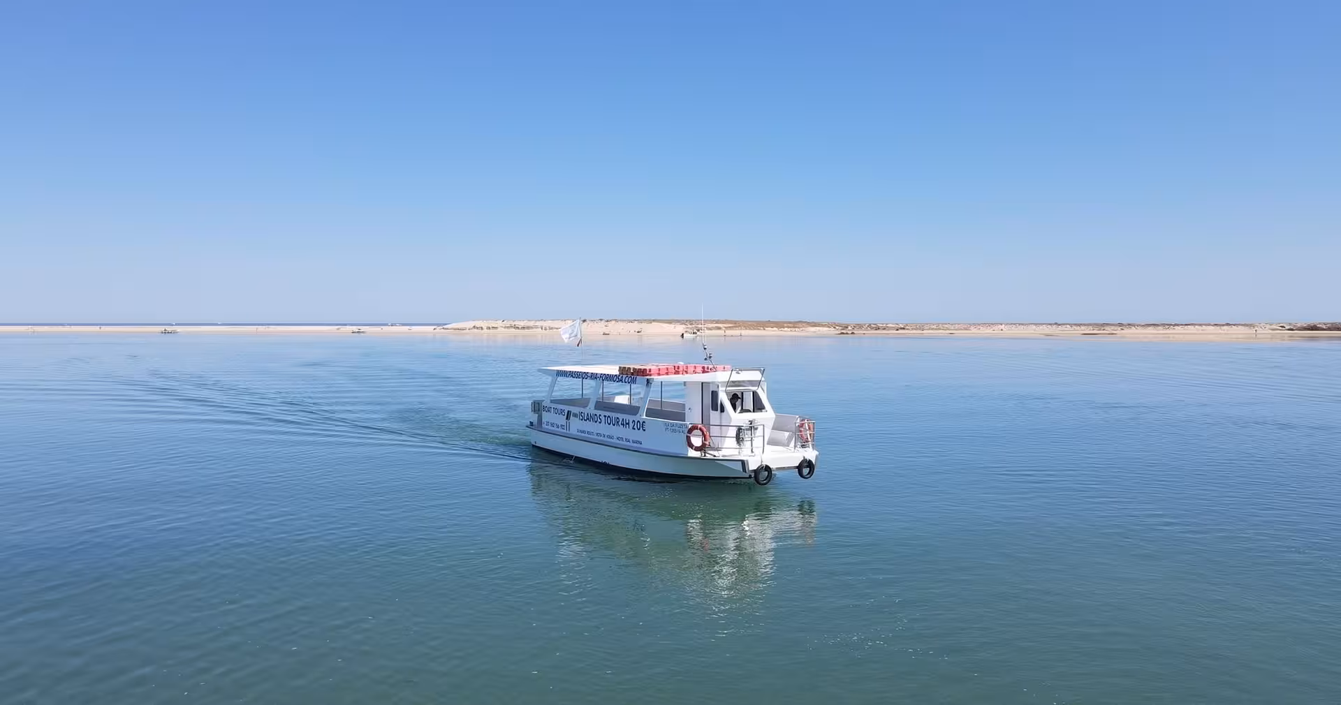 A white tour boat cruising the calm turquoise waters of Ria Formosa Natural Park near Olhao islands under a clear blue sky.