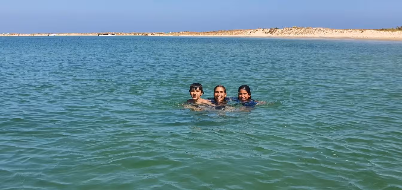 Three happy swimmers enjoying the clear waters of Ria Formosa, surrounded by scenic coastal beauty.