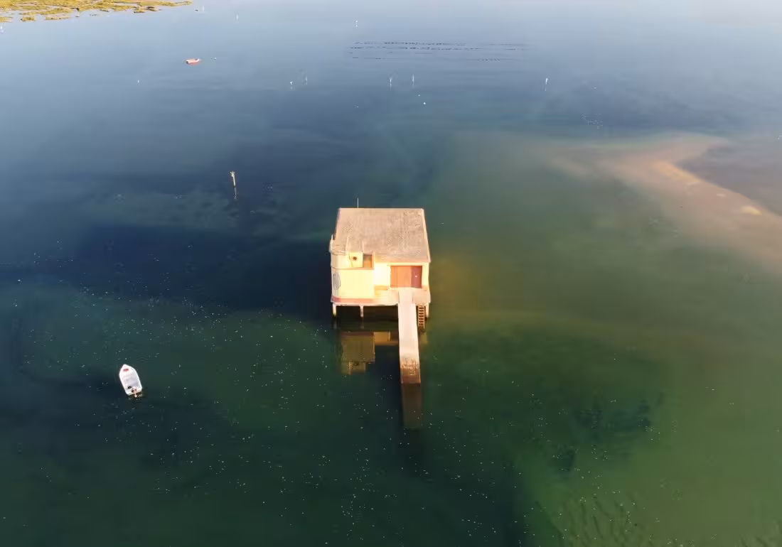 Aerial view of a traditional stilt house surrounded by the calm turquoise waters of Ria Formosa lagoon Algarve