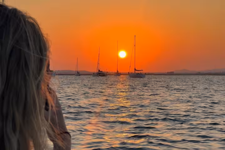 Traveler watching sunset over Ria Formosa with sailboats on calm water, Algarve sunset cruise tour view