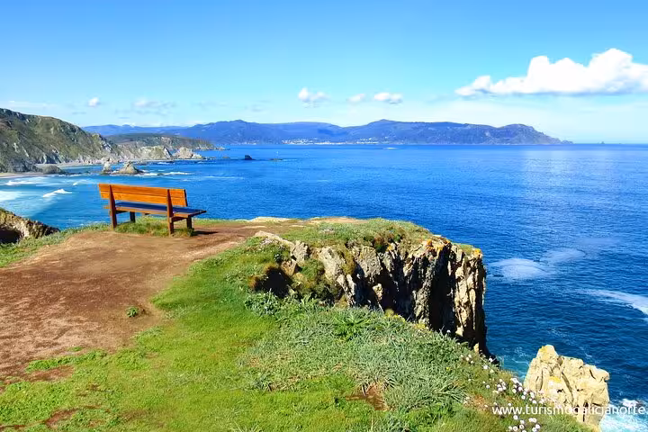 A solitary bench overlooking the breathtaking ocean and cliffs of Rías Altas under a clear blue sky.