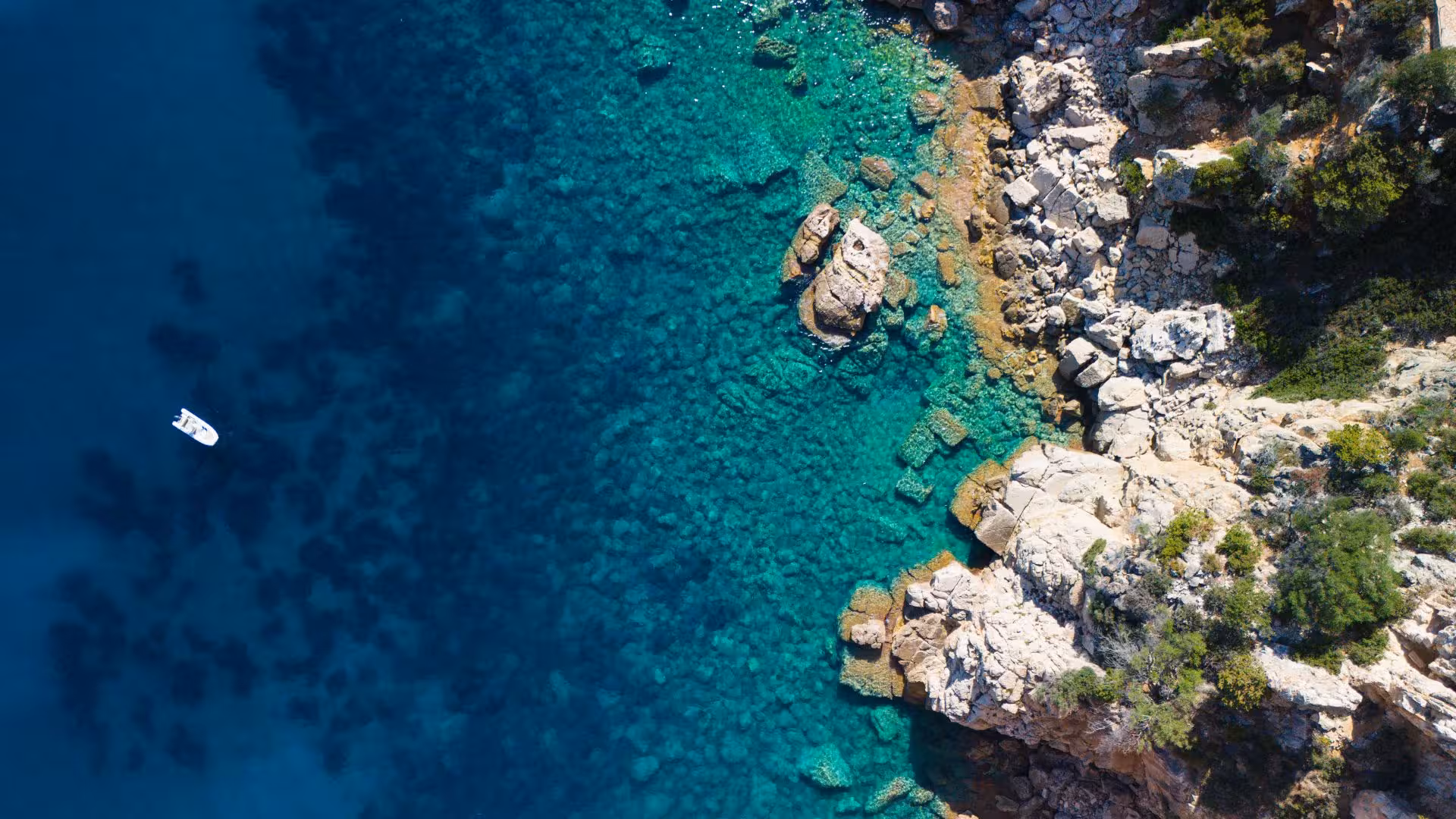 Aerial view of a small boat floating on the vibrant blue and turquoise waters near rocky shores on the Cala Goloritzé tour.