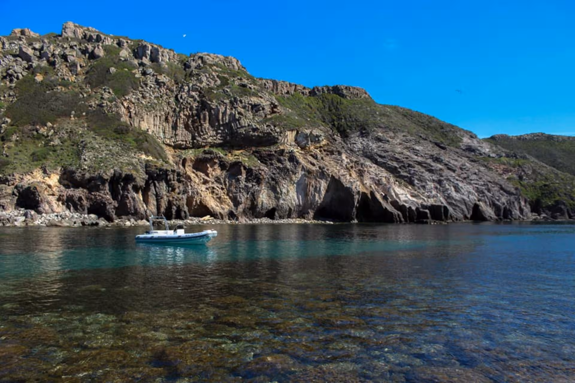 RIB boat floating near rocky cliffs on the Sant'Antioco tour between Carloforte and Masua.