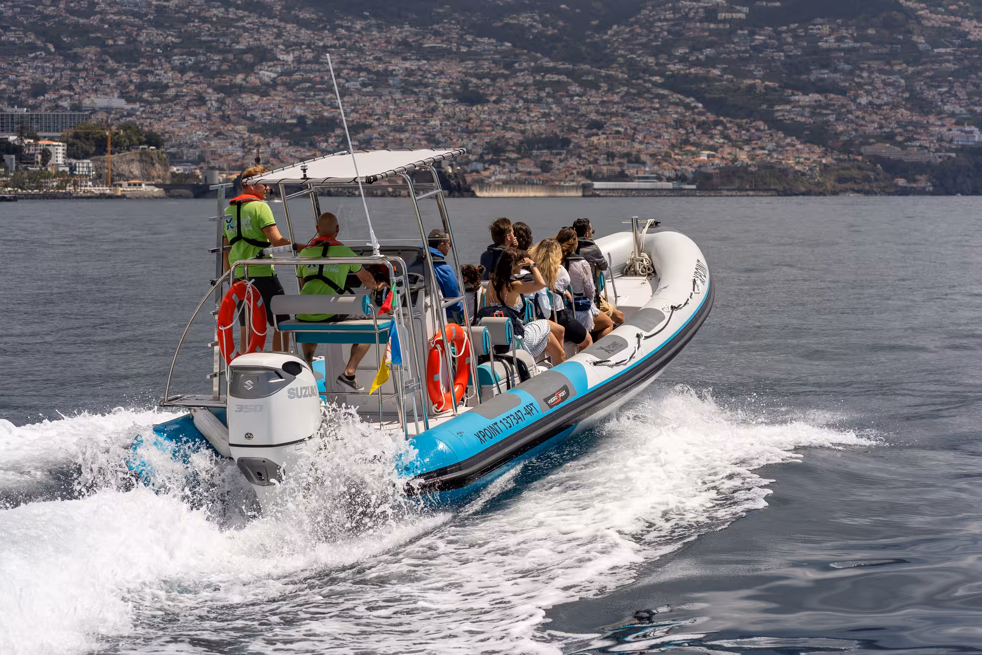RIB boat with tourists cruising near a coastal city, offering sunset views and optional dolphin and whale watching.
