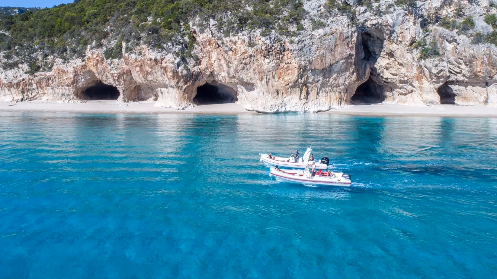 RIB boats near the stunning limestone caves of Cala Luna, with clear blue waters in the Gulf of Orosei, Sardinia.