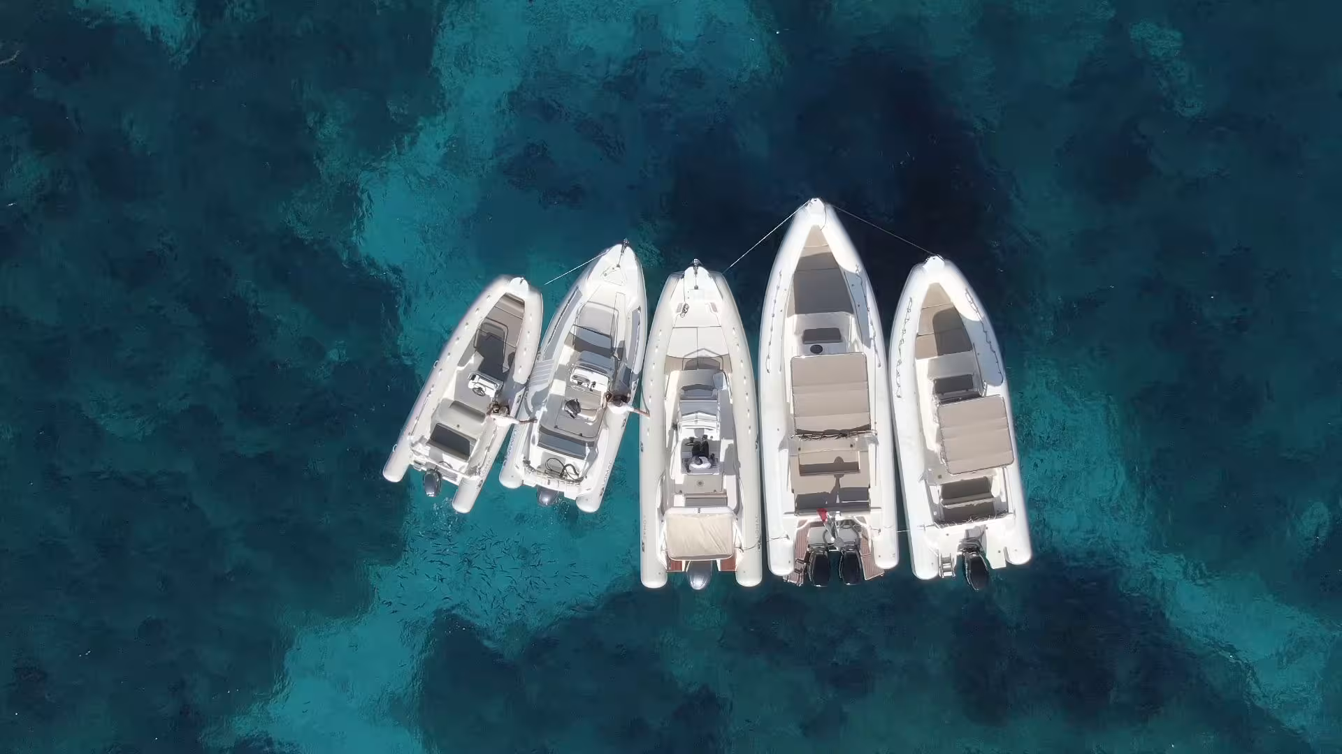 Aerial view of five RIB boats anchored together on the crystal-clear waters of the La Maddalena Archipelago.