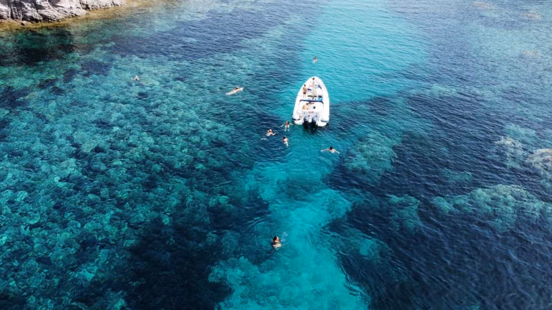 Aerial view of a RIB with swimmers in crystal clear waters near Sant'Antioco, perfect for Carloforte and Masua tours.