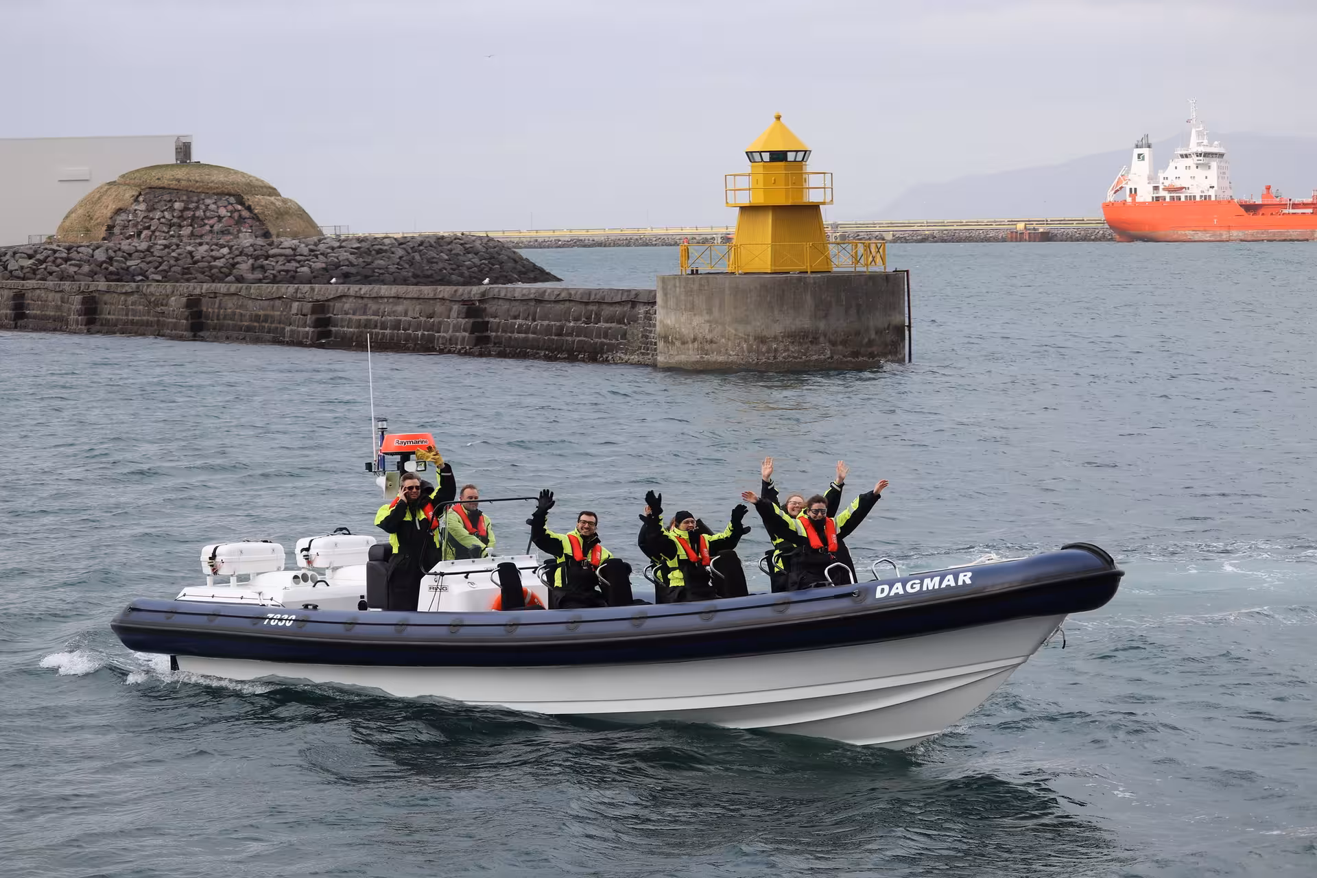 Group of tourists waving on RIB whale watching speedboat Dagmar near Reykjavik harbor lighthouse