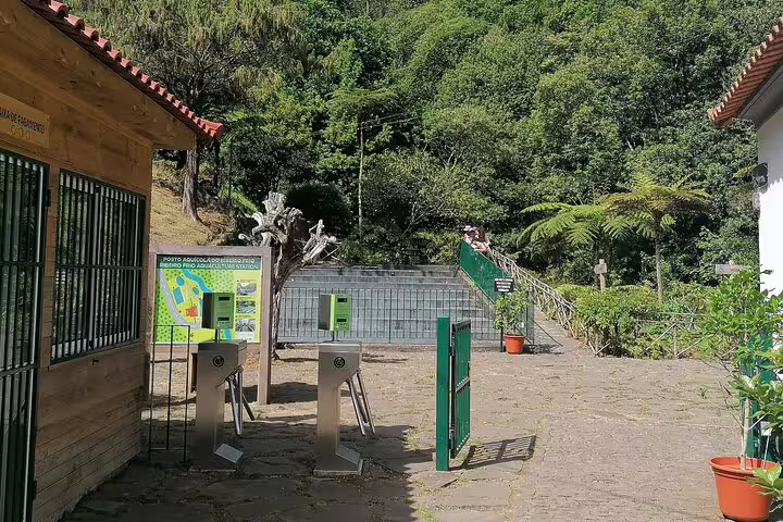 Entrance area of Ribeiro Frio with informational signs and turnstiles, set amidst lush green forest landscape.