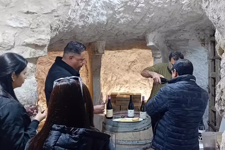 Visitors enjoying a wine tasting session in a rustic Ribera del Duero cellar, featuring bottles on a barrel table.