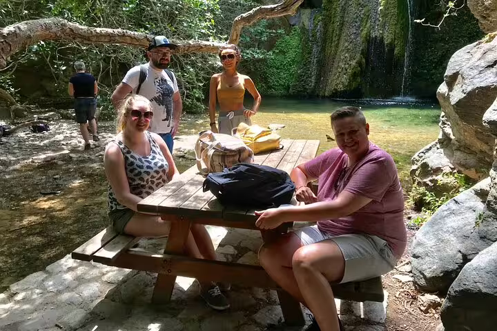 Group of tourists enjoying a picnic by Richti Waterfall, surrounded by lush greenery and serene waters.