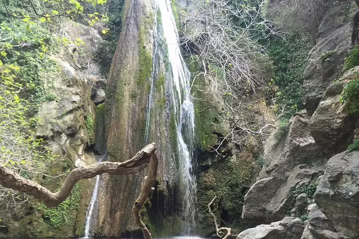 Majestic view of Richtis Waterfall cascading down a moss-covered cliff, framed by lush vegetation and rugged rocks.
