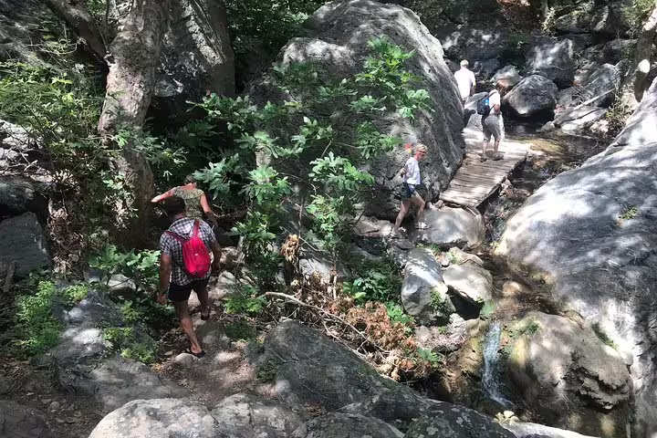 Hikers exploring the lush, rocky trail leading to Richtis Waterfall, surrounded by dense greenery and natural beauty.