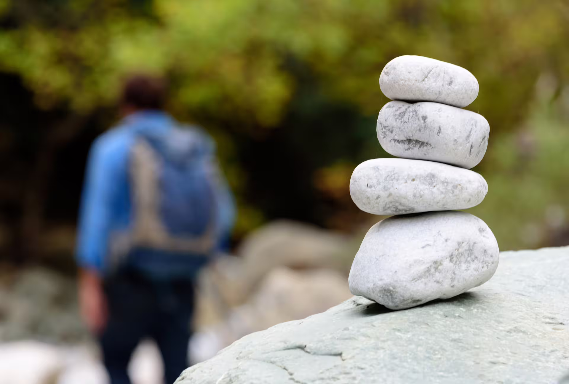 Stacked river stones beside the Ridomo Gorge path with blurred hiker, peaceful nature hike in Taygetos, Greece