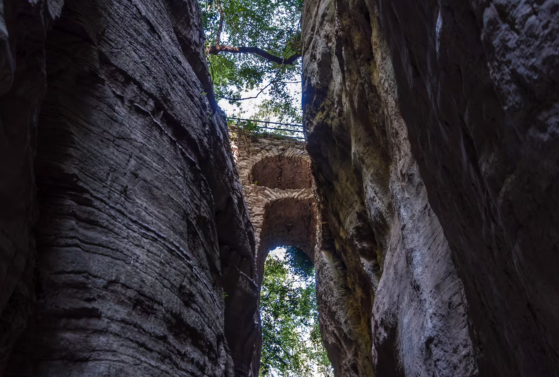Looking up at stone bridge between towering cliffs in Ridomo Gorge, a dramatic hiking canyon in Greece