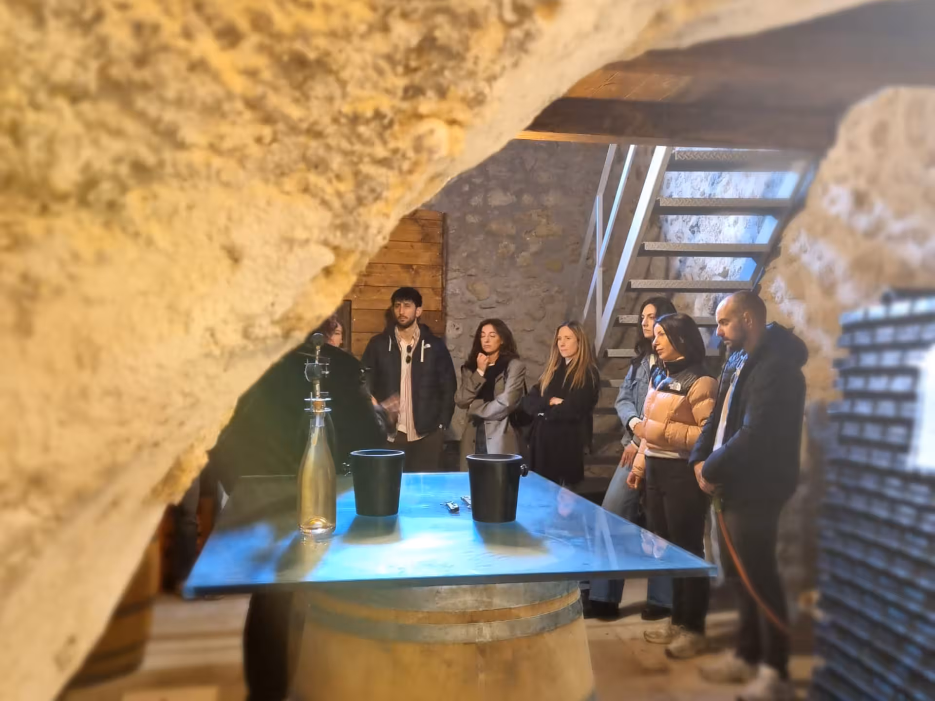 Group of tourists exploring a rustic wine cellar in Rieti, with stone walls and wine barrels on display.