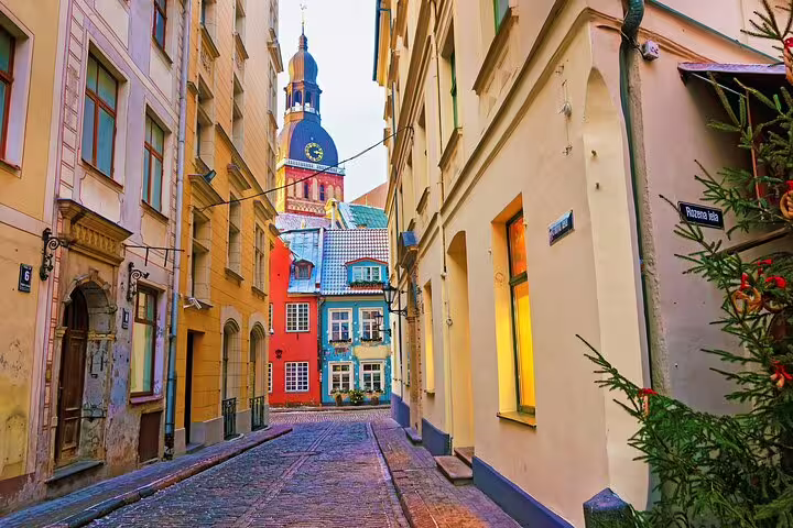 Narrow cobblestone street in Riga Old Town with colorful buildings and cathedral tower in background
